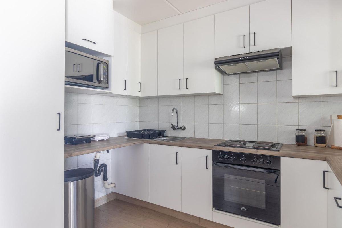 Compact kitchen featuring white cabinetry, wood-look countertops, built-in oven, gas hob, and extractor fan with tiled splashback.