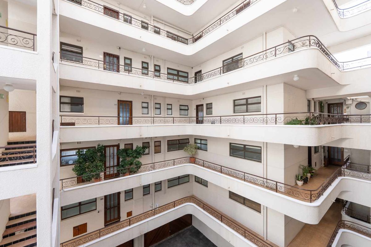 A multi-level apartment building featuring a central atrium design with open-air walkways and decorative wrought iron railings on each floor.