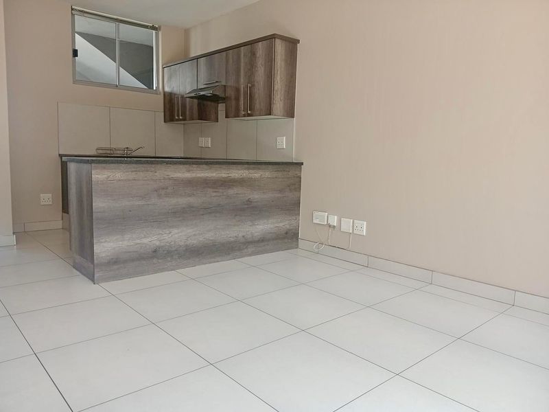 A modern, empty kitchen featuring wood-finish cabinetry, stone countertops, an integrated extractor fan, and clean tiled flooring.