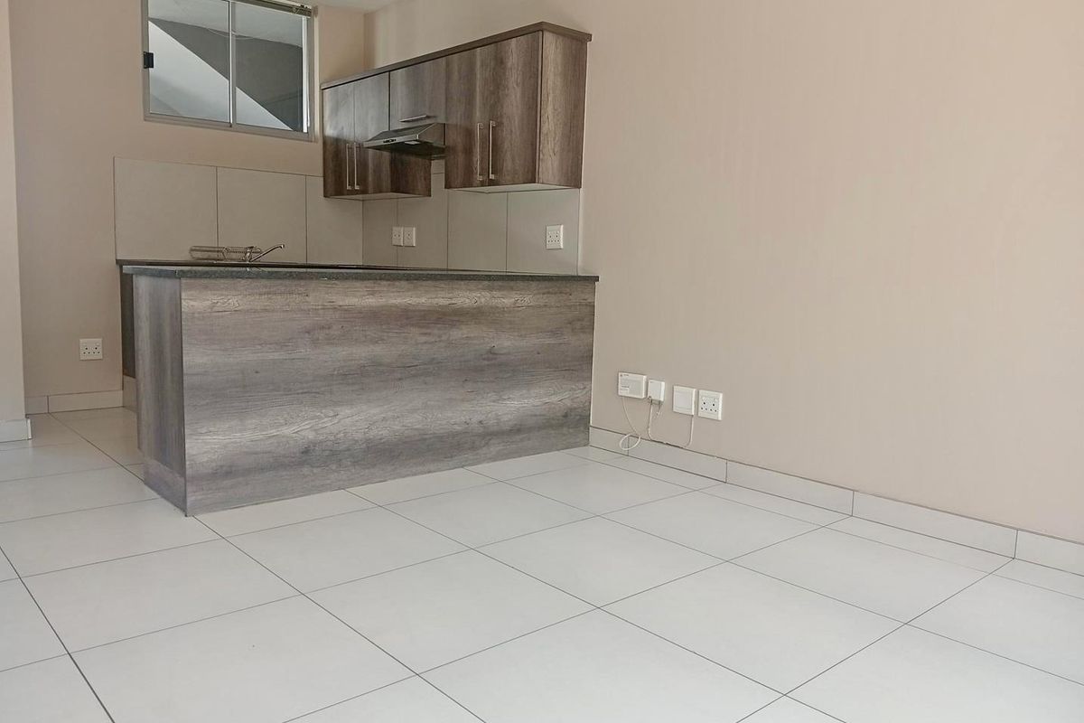 A modern, empty kitchen featuring wood-finish cabinetry, stone countertops, an integrated extractor fan, and clean tiled flooring.