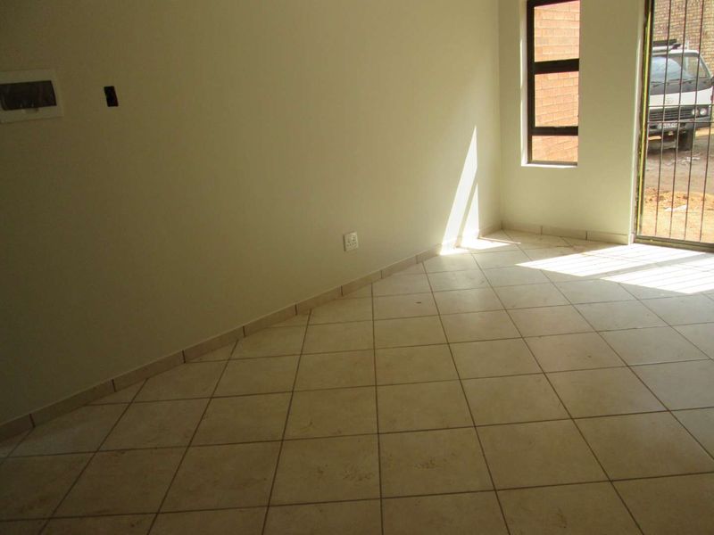 An empty living area featuring neutral ceramic floor tiles, tiled skirting, and a large window with an integrated security gate.
