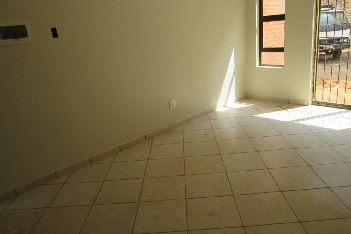 An empty living area featuring neutral ceramic floor tiles, tiled skirting, and a large window with an integrated security gate.