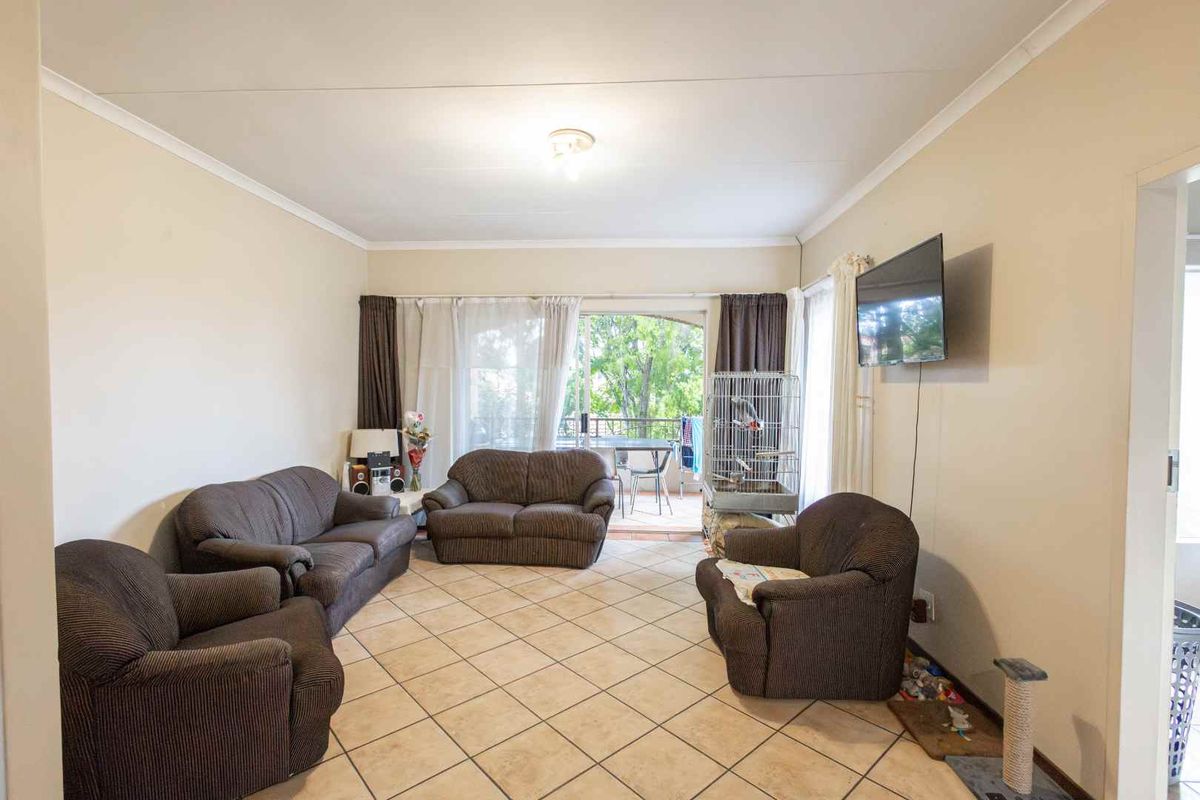 A spacious living room featuring neutral tiled flooring and direct access to an outdoor balcony area through sliding glass doors.
