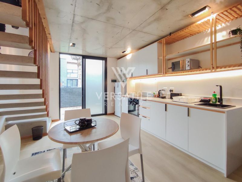 Modern open-plan kitchen and living area featuring an exposed concrete ceiling, sleek cabinetry, integrated appliances, and a timber staircase leading to the upper level.