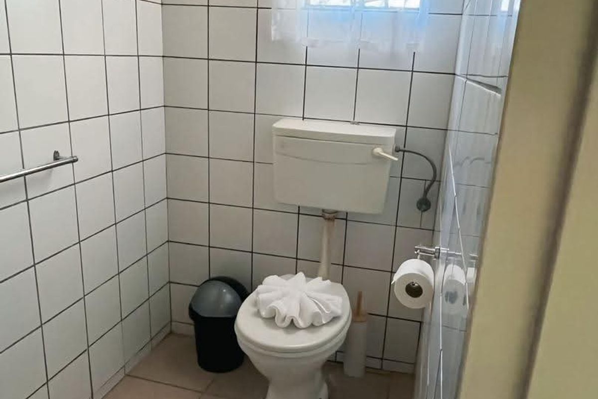 A compact hotel bathroom featuring white wall tiles, a standard toilet, and a small window with natural light.
