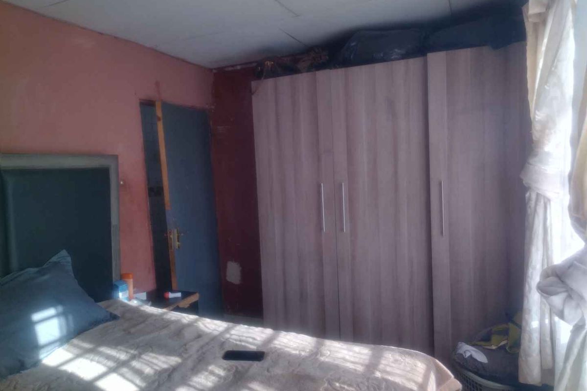 A bedroom featuring built-in wooden wardrobes and a standard door, requiring cosmetic updates to the wall and ceiling finishes.