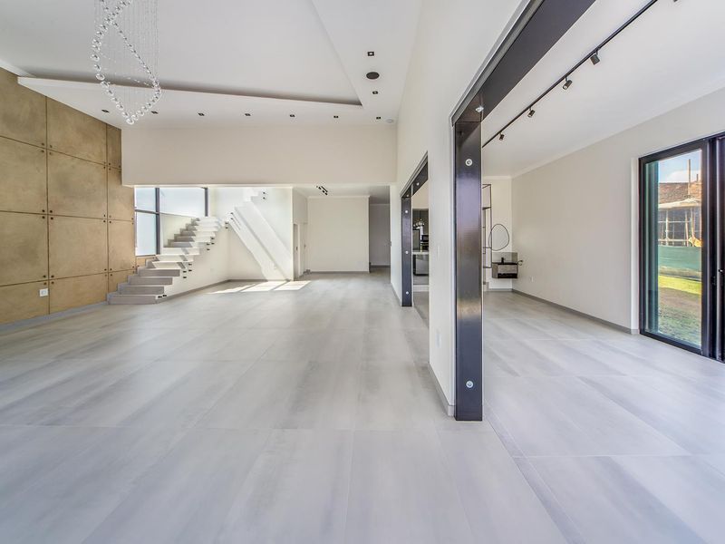 Spacious open-plan living area featuring modern tiled flooring, a striking feature wall, architectural staircase, and large sliding doors leading to the exterior.