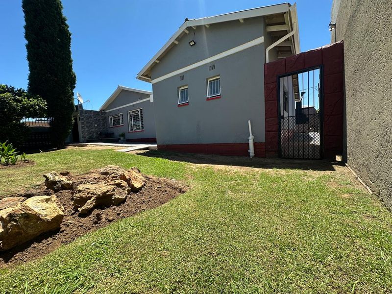 Rear exterior view of the house featuring a lawn, paved walkway, security gate, and window security bars.
