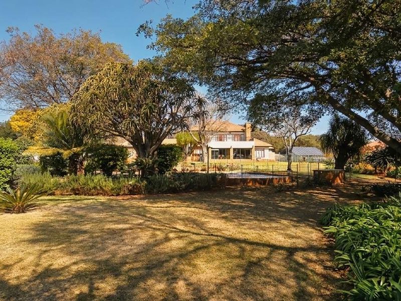 A spacious, well-maintained garden featuring mature trees, established landscaping, and a swimming pool area with a view of the rear house elevation.