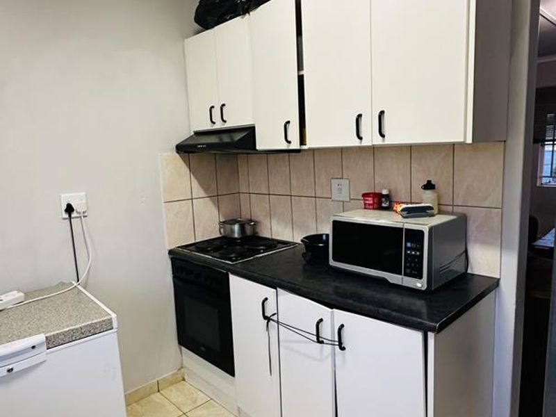 Compact kitchen featuring white cabinetry, dark laminate countertops, ceramic tile backsplash, and tiled flooring, equipped with a built-in oven and hob.