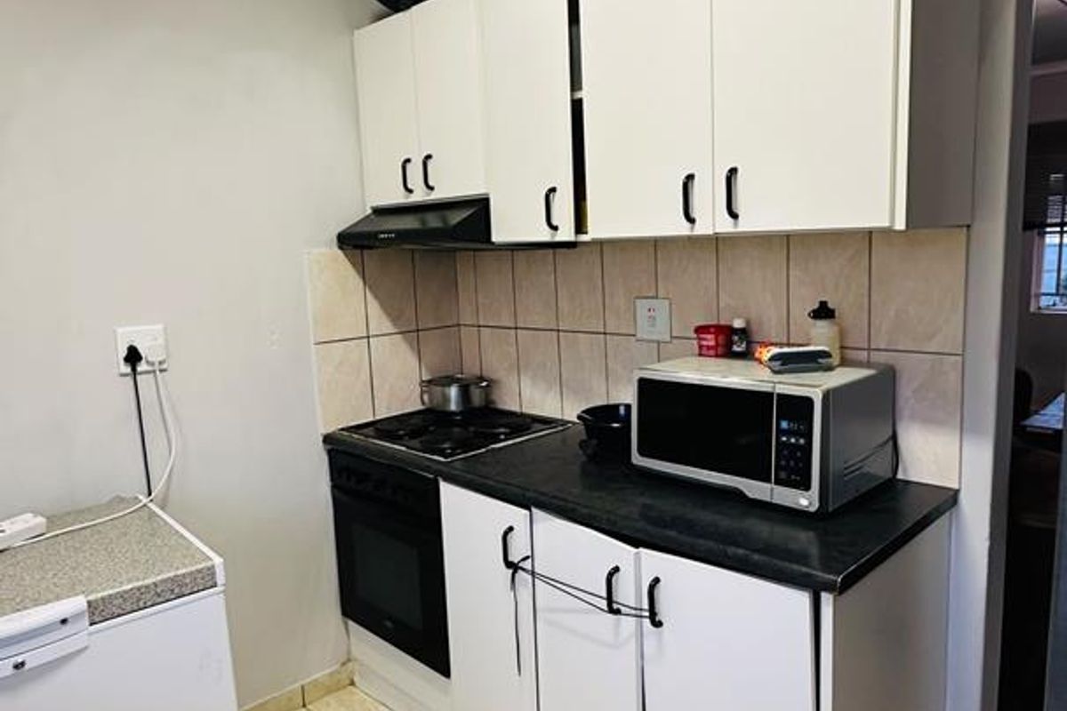 Compact kitchen featuring white cabinetry, dark laminate countertops, ceramic tile backsplash, and tiled flooring, equipped with a built-in oven and hob.