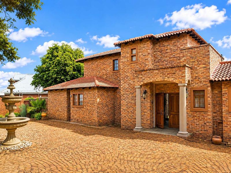 A charming double-story brick home featuring a classic tiled roof, stone columns at the entrance, and a decorative stone fountain in the front courtyard.