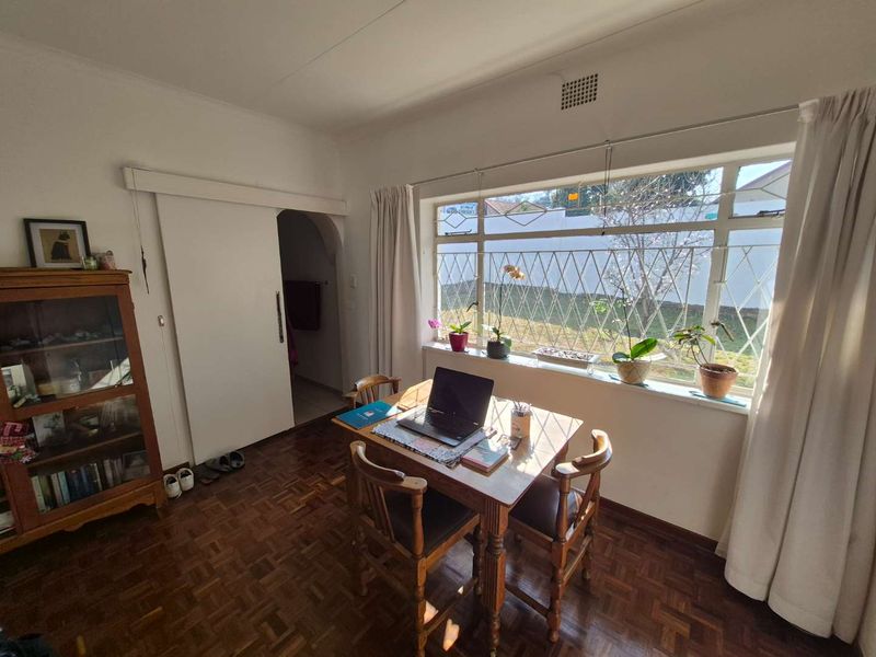 A bright living area featuring classic parquet flooring, a large window with security bars, and a sliding door leading to an adjacent space.