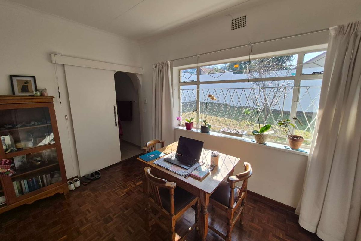 A bright living area featuring classic parquet flooring, a large window with security bars, and a sliding door leading to an adjacent space.