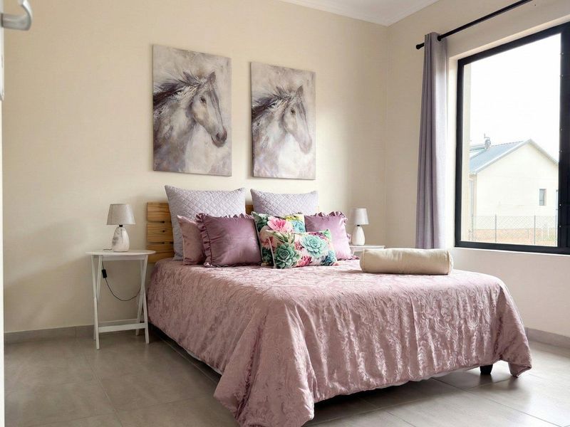 A well-lit bedroom featuring neutral tiled flooring and a large window, providing a clean and comfortable living space.