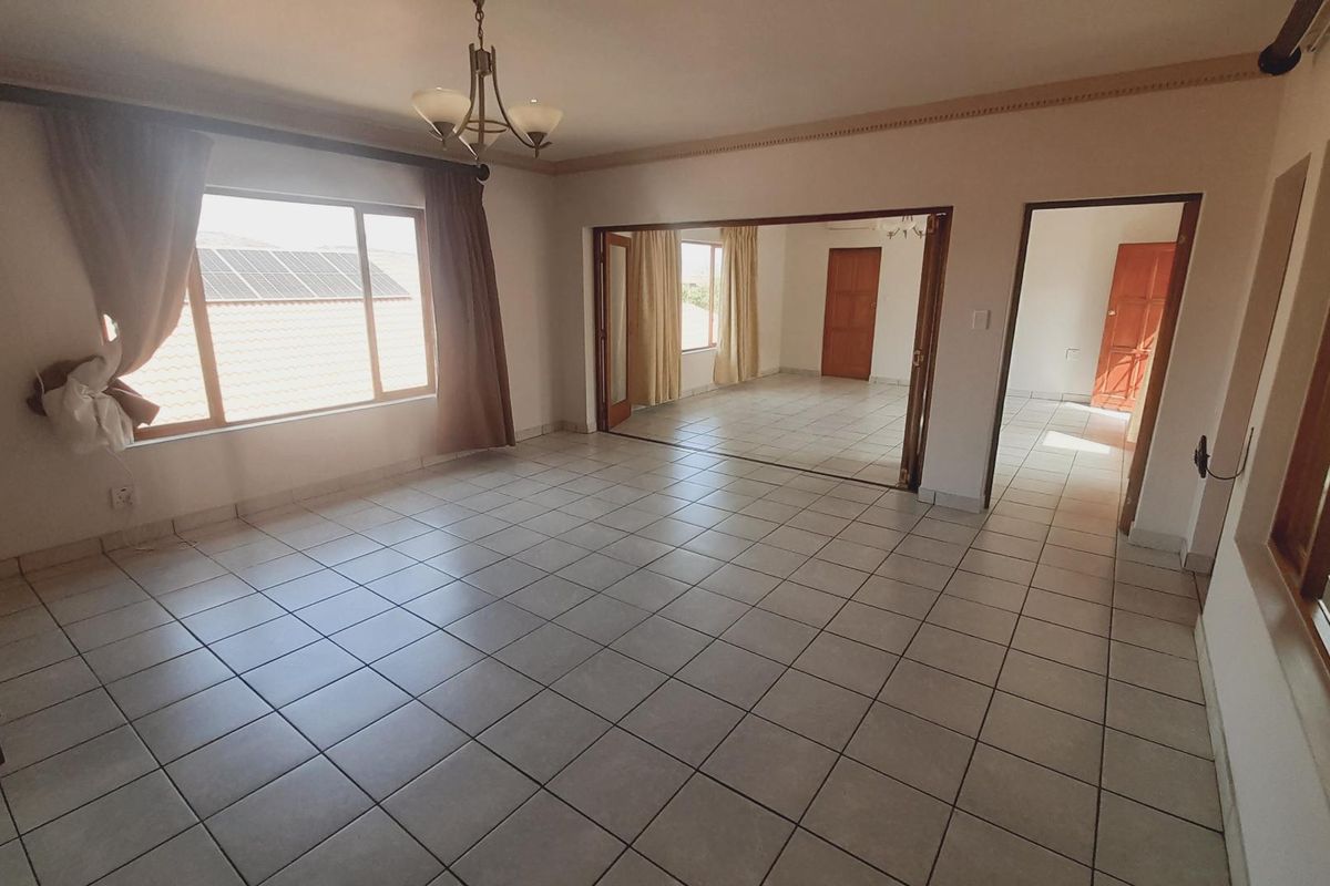 Spacious living area featuring neutral ceramic floor tiles, large windows for natural light, and direct access to an adjoining room through double doors.