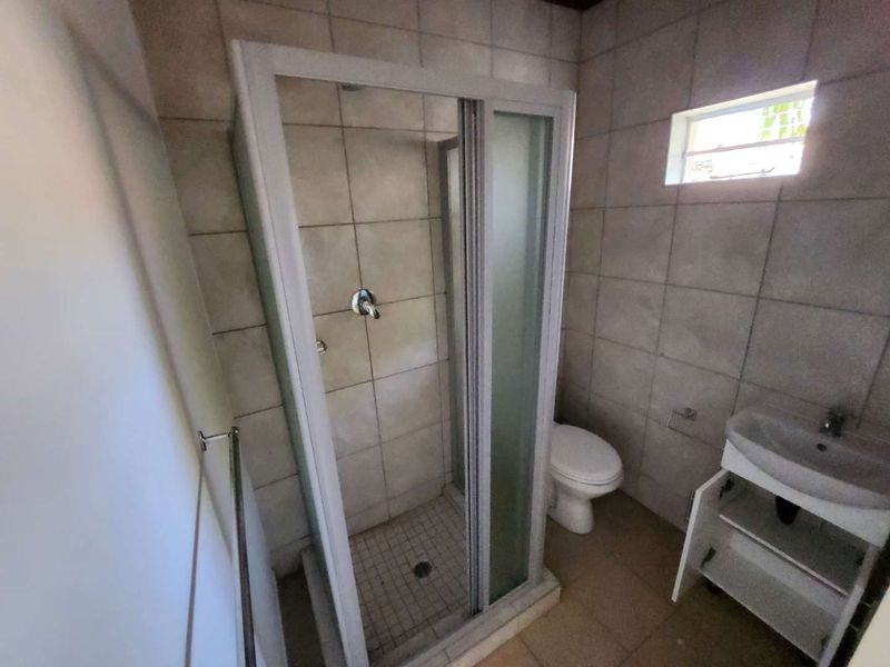 A functional bathroom featuring a shower enclosure, toilet, and vanity basin with tiled finishes throughout.