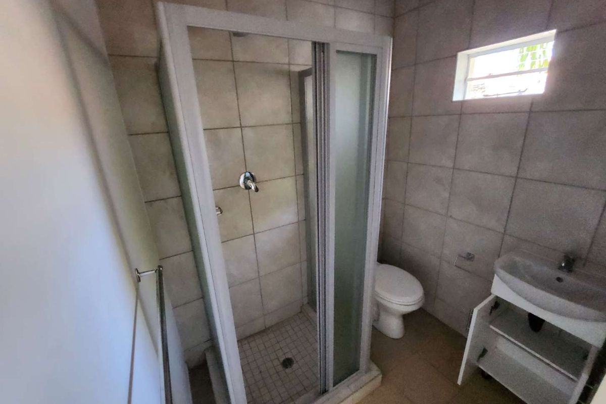 A functional bathroom featuring a shower enclosure, toilet, and vanity basin with tiled finishes throughout.