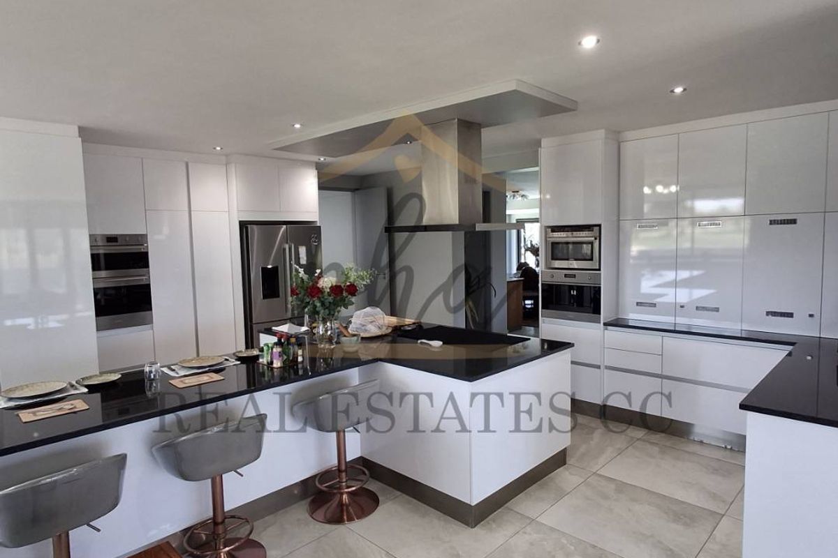 Modern kitchen featuring high-gloss cabinetry, black stone countertops, a central island with breakfast bar, and integrated stainless steel appliances.
