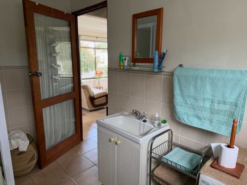 A functional bathroom featuring a vanity cabinet with a ceramic basin, tiled splashback, and a wall-mounted mirror, with direct access to an adjacent living area.