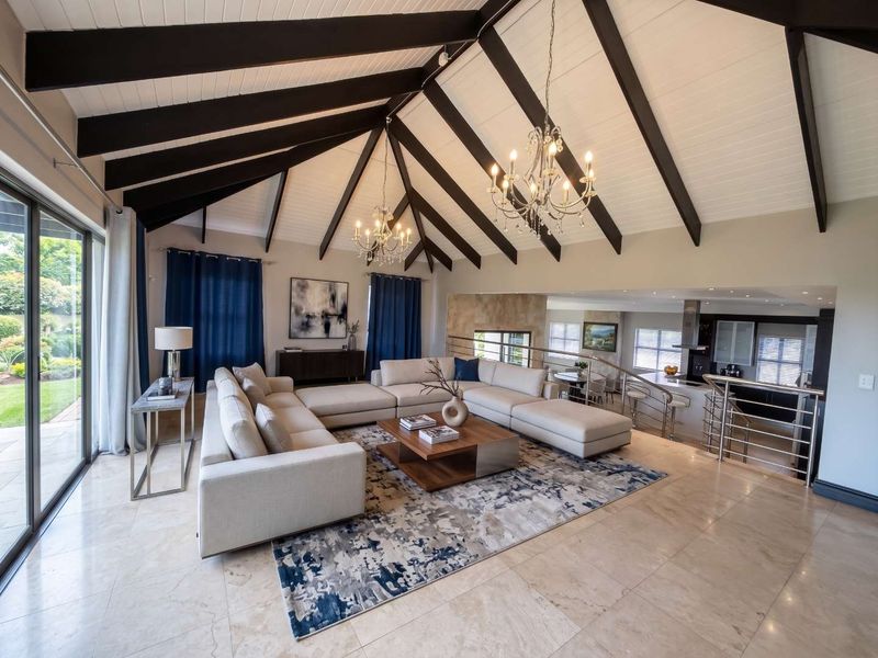 Spacious open-plan living area featuring vaulted ceilings with exposed beams, stone flooring, and seamless flow to the kitchen and outdoor patio area.