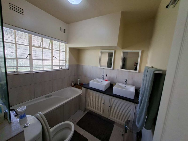 A functional bathroom featuring a double vanity with vessel sinks, a built-in bathtub, and neutral wall tiling.