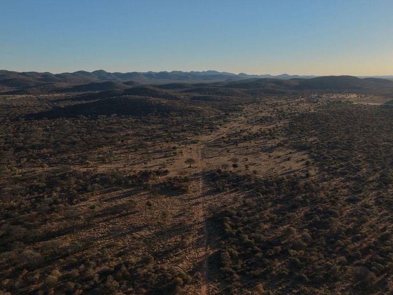 An expansive aerial view of the lodge's surrounding savanna landscape, featuring a dirt access road stretching through the natural bushveld terrain.