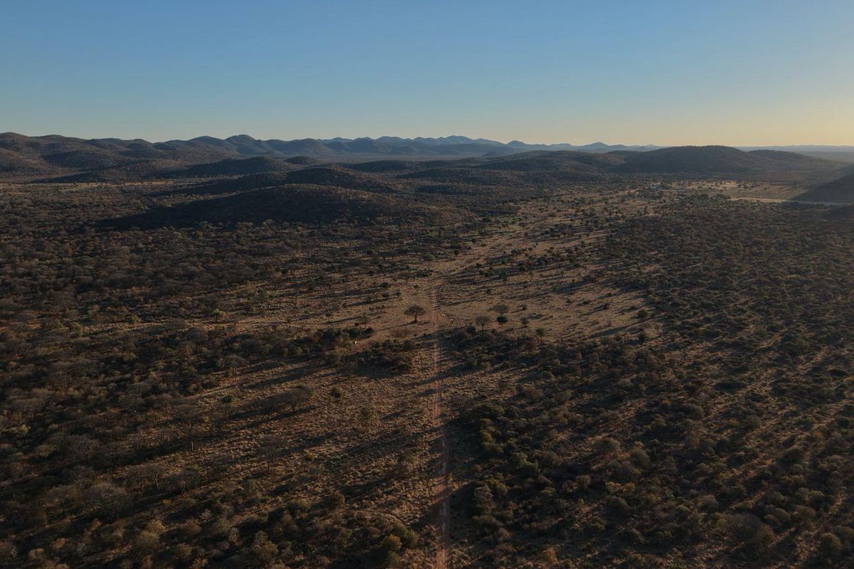 An expansive aerial view of the lodge's surrounding savanna landscape, featuring a dirt access road stretching through the natural bushveld terrain.