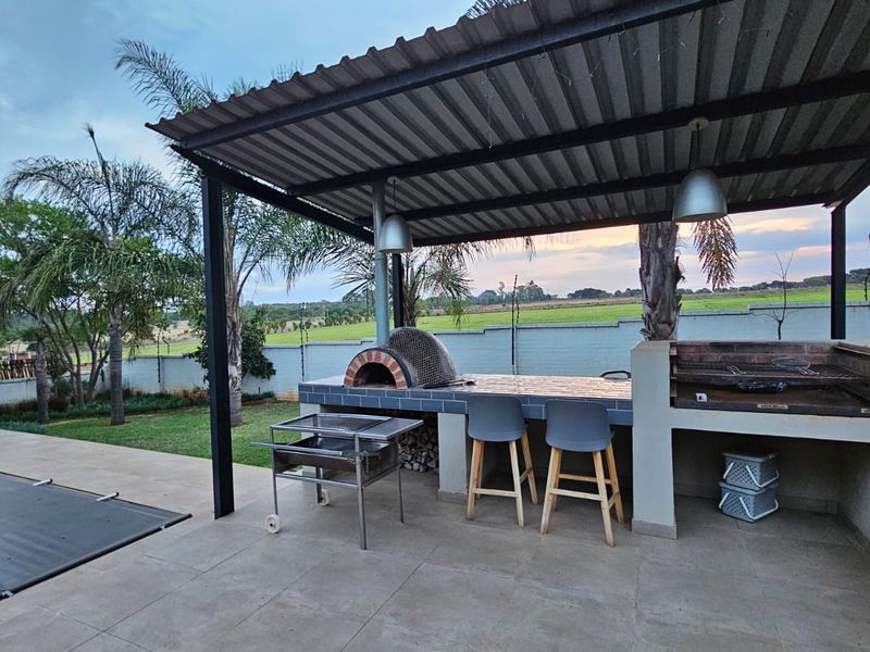 Covered outdoor entertainment area featuring a built-in pizza oven, braai station, tiled prep surfaces, and pendant lighting overlooking the garden.