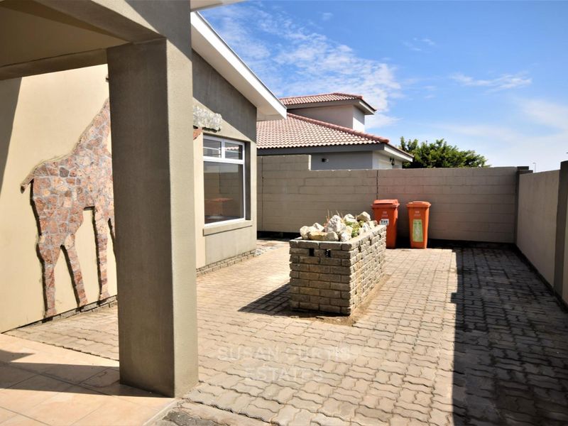 A paved rear courtyard featuring a brick planter box, covered patio area, and masonry boundary walls.