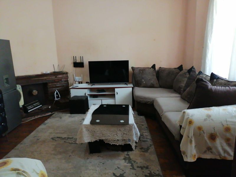 A living room featuring a brick fireplace and hardwood flooring, currently furnished with a sectional sofa and media unit.
