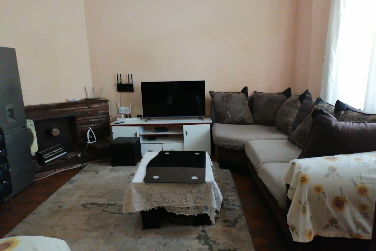 A living room featuring a brick fireplace and hardwood flooring, currently furnished with a sectional sofa and media unit.