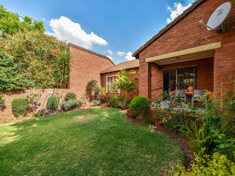 A private rear garden featuring a well-maintained lawn, established landscaping, and a covered patio area with direct access to the townhouse interior.