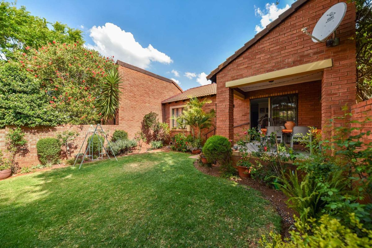 A private rear garden featuring a well-maintained lawn, established landscaping, and a covered patio area with direct access to the townhouse interior.