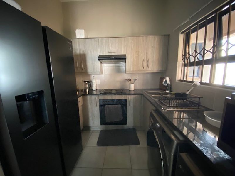 A functional kitchen featuring light wood-finish cabinetry, granite countertops, a built-in oven with hob, and an extractor fan, complemented by tiled flooring.