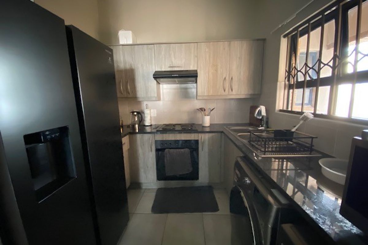 A functional kitchen featuring light wood-finish cabinetry, granite countertops, a built-in oven with hob, and an extractor fan, complemented by tiled flooring.