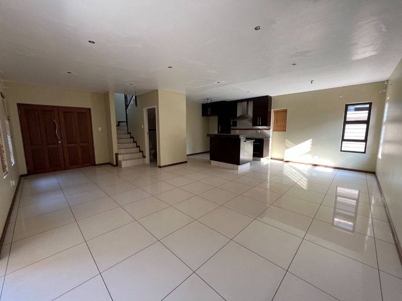 Spacious open-plan living area featuring large format floor tiles, recessed lighting, and a modern kitchen with built-in cabinetry and an island.