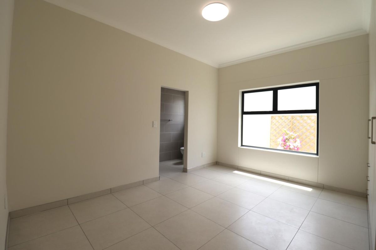 A clean, vacant bedroom featuring neutral tiled flooring, built-in cupboards, and an en-suite bathroom, offering a bright and modern blank canvas.