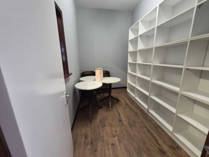A compact office space featuring built-in white shelving units and wood-look laminate flooring.