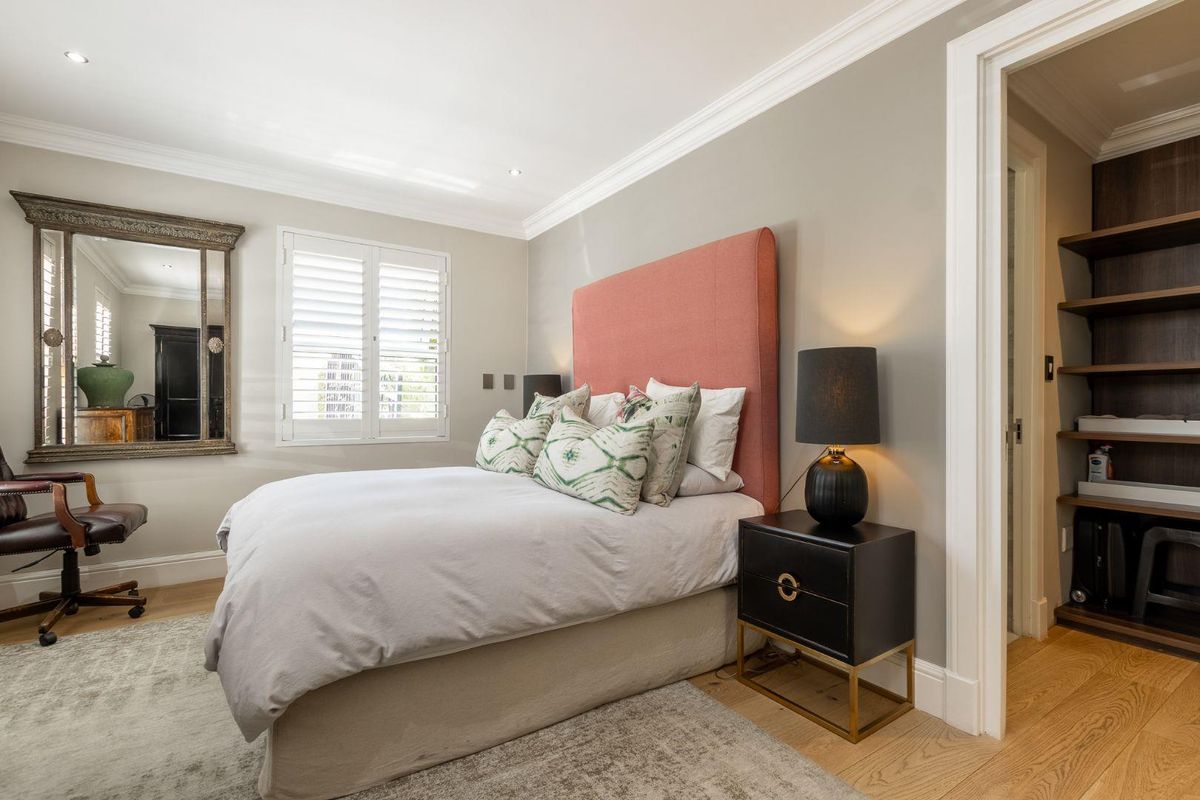 A well-appointed bedroom featuring crown molding, plantation shutters, and an adjoining walk-in closet with custom shelving.