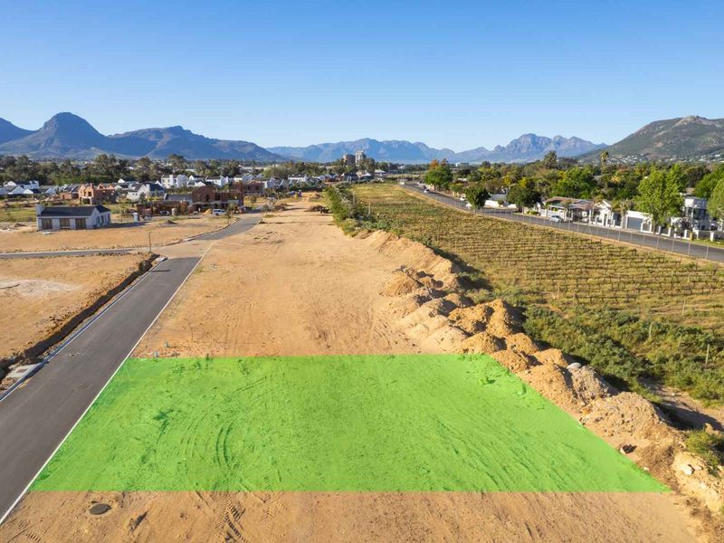 Aerial view of a vacant residential plot in a developing estate, featuring road access and surrounding mountain views.