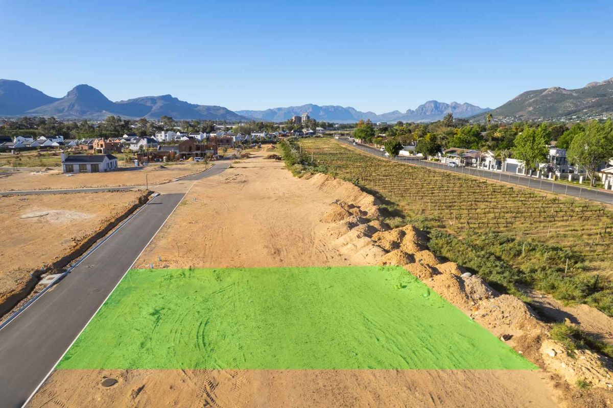 Aerial view of a vacant residential plot in a developing estate, featuring road access and surrounding mountain views.