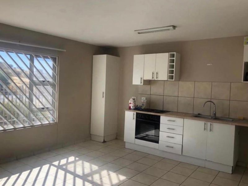 A functional kitchen featuring built-in cabinetry, a tiled backsplash, and integrated oven and hob, with tiled flooring and security bars on the window.
