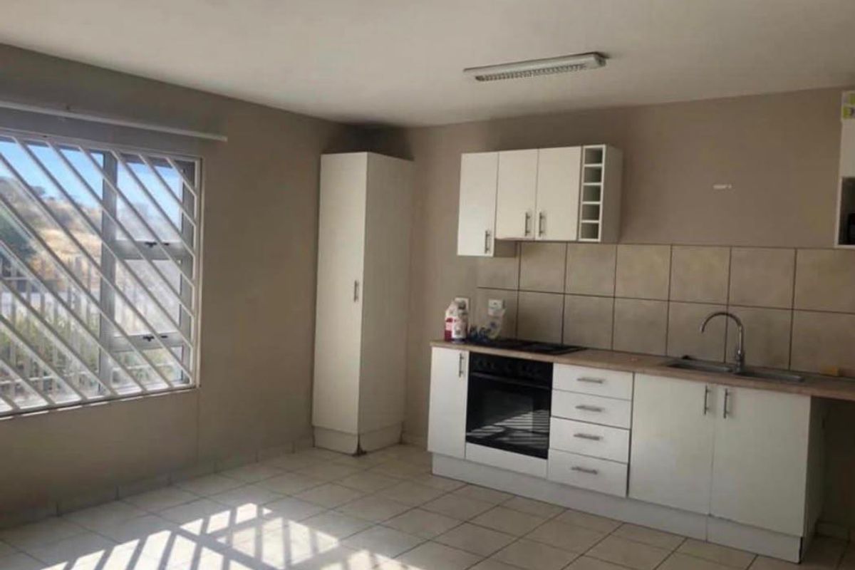 A functional kitchen featuring built-in cabinetry, a tiled backsplash, and integrated oven and hob, with tiled flooring and security bars on the window.
