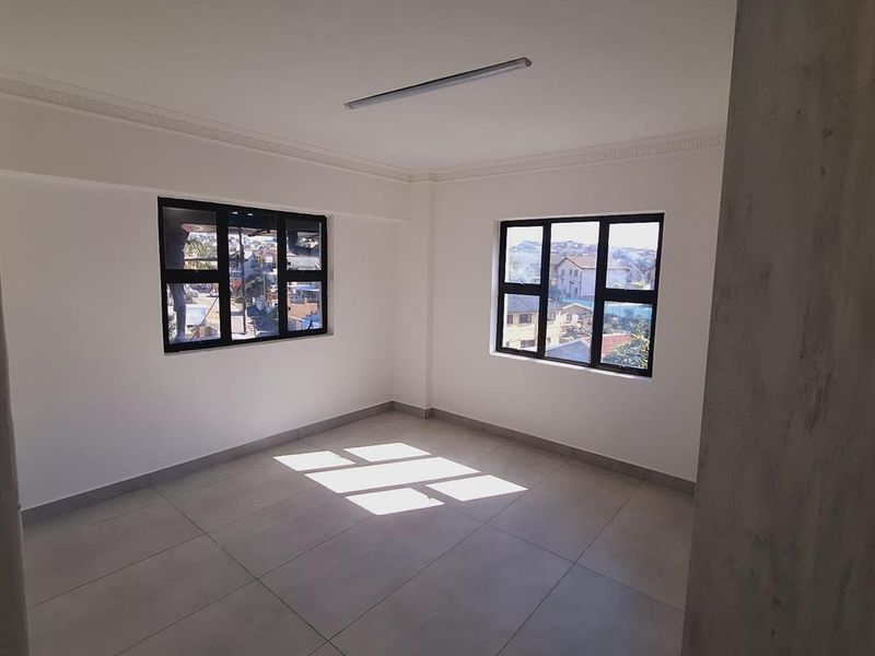 A bright, empty bedroom featuring neutral tiled flooring, modern black aluminium window frames, and a built-in cupboard.