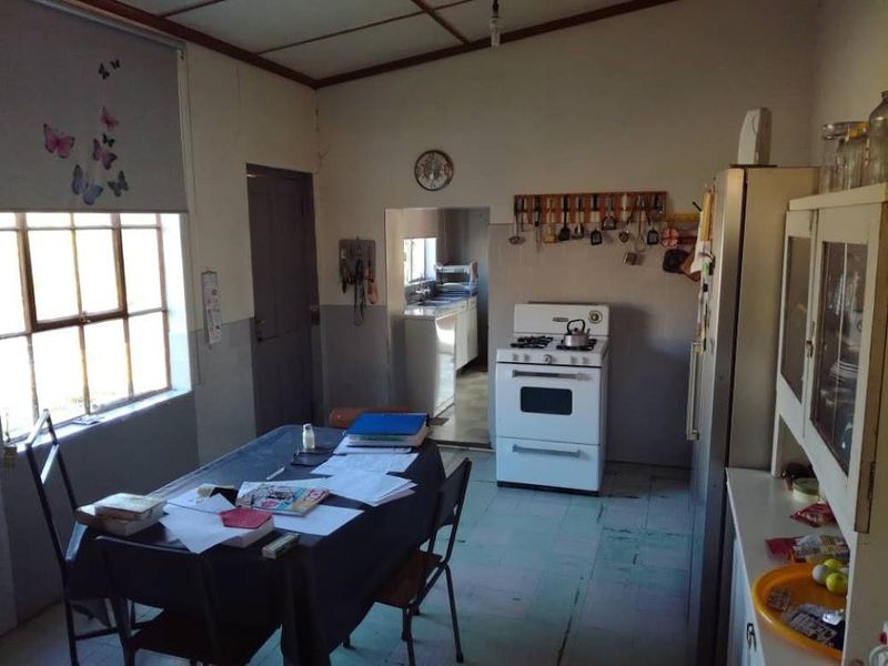 A dated kitchen featuring a freestanding stove, tiled flooring, and an adjacent scullery area, offering a functional layout with potential for modernization.