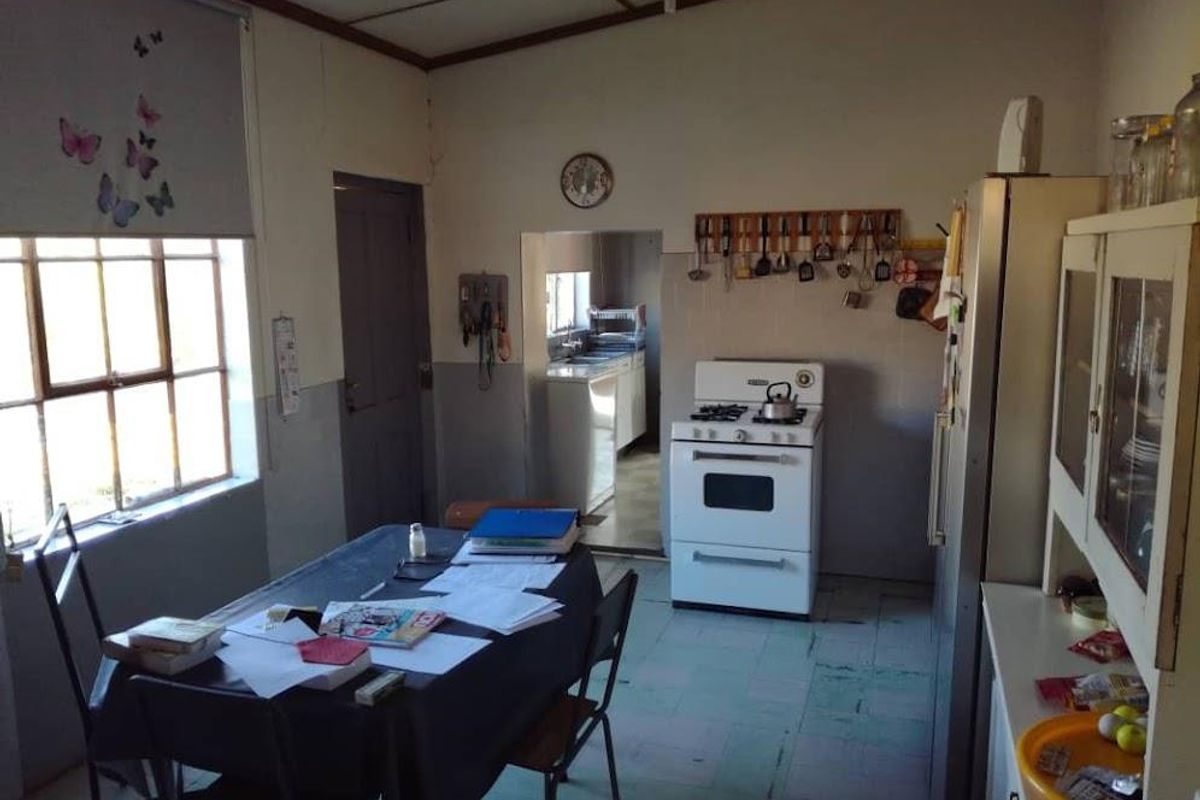 A dated kitchen featuring a freestanding stove, tiled flooring, and an adjacent scullery area, offering a functional layout with potential for modernization.