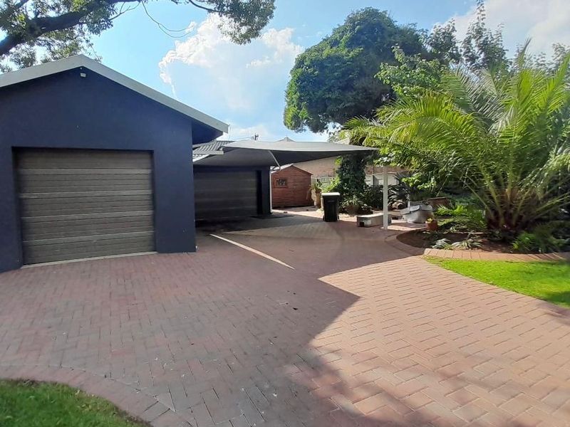 A well-maintained front exterior featuring a double garage, paved driveway, and established garden with a shade sail covering the parking area.