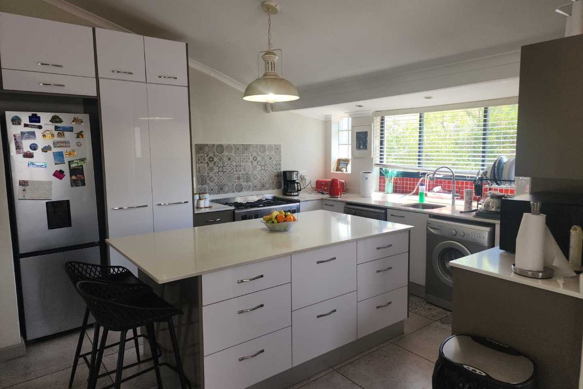 Modern kitchen featuring a central island with stone countertop, white cabinetry, integrated gas hob, and tiled backsplash, offering a functional and bright cooking space.