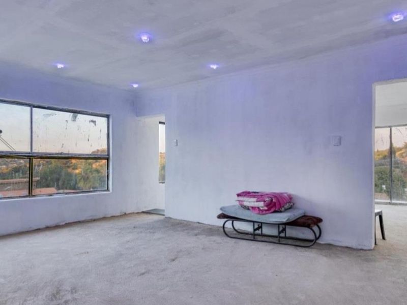 An unfinished, vacant living area featuring recessed lighting and large windows with views, requiring final flooring and wall finishing to complete the space.